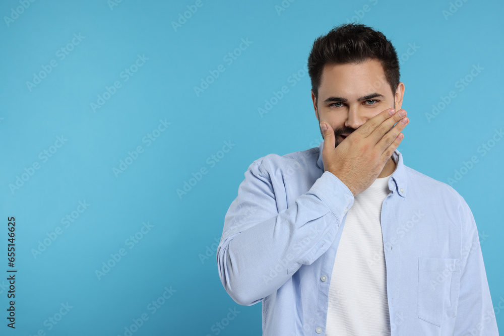 Embarrassed man covering mouth on light blue background. Space for text Embarrassed man covering mouth on light blue background. Space for text