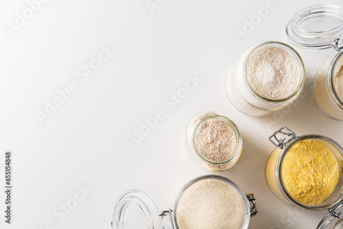 food storage, culinary and eating concept - close up of jars with different kind of flour on white background, top view