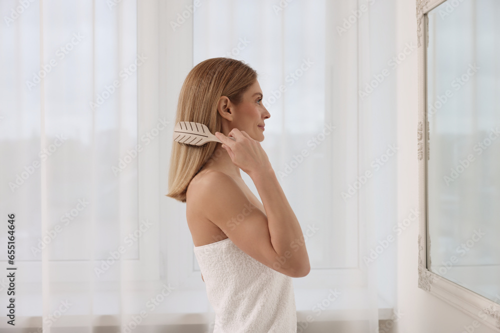 Beautiful woman brushing her hair near mirror in room Beautiful woman brushing her hair near mirror in room