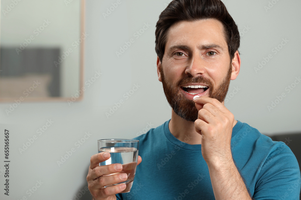 Handsome man with glass of water taking pill indoors, space for text - obrazy, fototapety, plakaty 