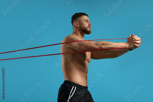 Muscular man exercising with elastic resistance band on light blue background