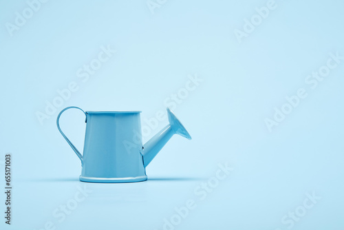 Bright blue garden watering can on the surface of the bright solid fond plain bright blue background photo