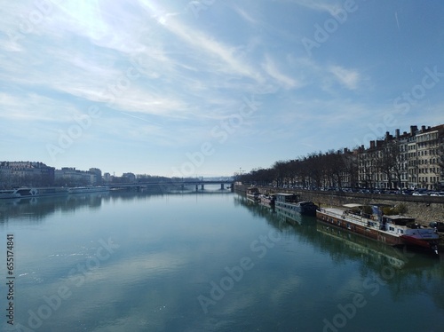 Seen on the banks of the Rhone, with moored boats, the bridge that spans the river, and the buildings on the other bank a sunny day in Lyon. France