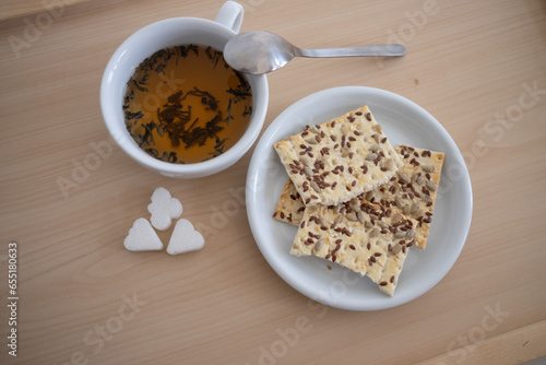 a cup of tea is on the table, and there are cookies in a saucer next to it. Sugar is on the table. Breakfast. tinting