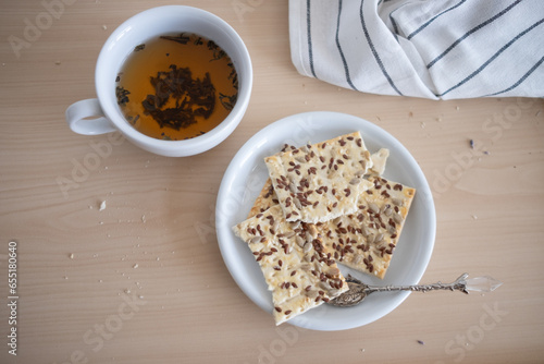 a cup of tea is on the table, and there are cookies in a saucer next to it. Sugar is on the table. Breakfast. tinting