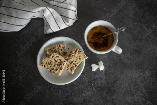 a cup of tea is on the table, and there are cookies in a saucer next to it. Sugar is on the table. Breakfast. tinting