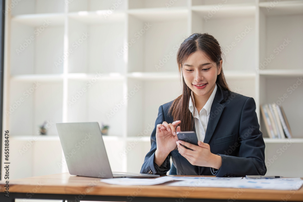 Attractive Asian woman using laptop in online meeting. Businesswoman using mobile phone talking with colleague sitting at table in modern office Attractive Asian woman using laptop in online meeting. Businesswoman using mobile phone talking with colleague sitting at table in modern office