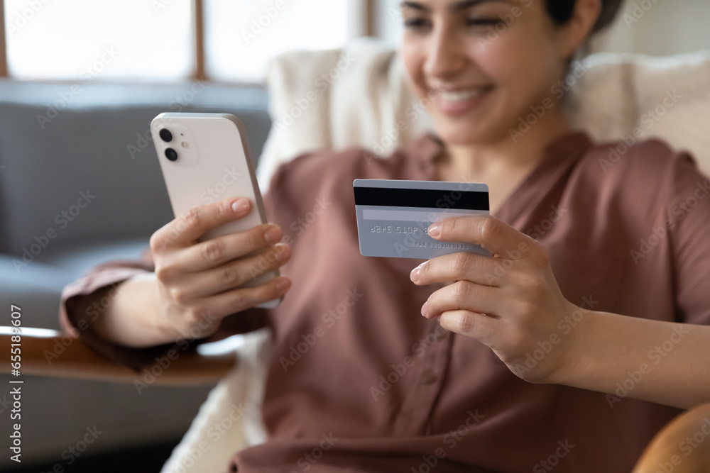 Close up smiling Indian woman paying online, using smartphone, focus on mobile device and credit card in happy young female hands, browsing internet banking service, shopping, purchasing goods Close up smiling Indian woman paying online, using smartphone, focus on mobile device and credit card in happy young female hands, browsing internet banking service, shopping, purchasing goods