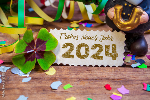 Wooden hang tag and slate with four leaf clover and sparklers with the german words for happy new year - frohes neues jahr 2024 on wooden weathered background © Stockwerk-Fotodesign