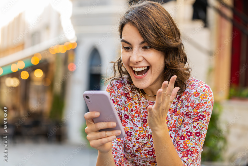 Portrait of woman use mobile smartphone celebrating win good message news lottery jackpot victory giveaway online play game outdoors. Happy girl tourist standing in urban city street. Town lifestyles