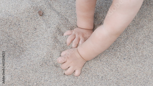 Baby enjoying putting his hands in sand at a beach.