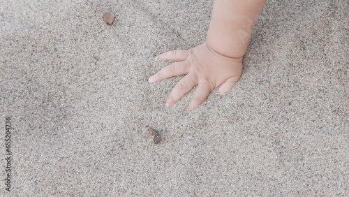 Baby enjoying putting his hands in sand at a beach.