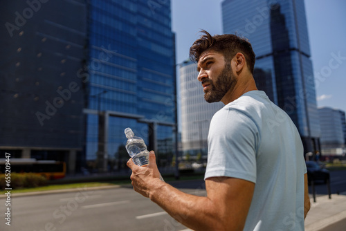 Fényképezés Sport man drinking water after running in the city skyscrapers background and lo