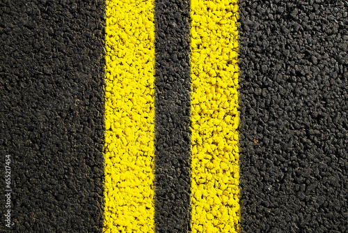 Close-up yellow dividing lines on the road with copy space. Yellow double solid line. Road markings on asphalt. Gray asphalt background with two yellow road lines. Black asphalt