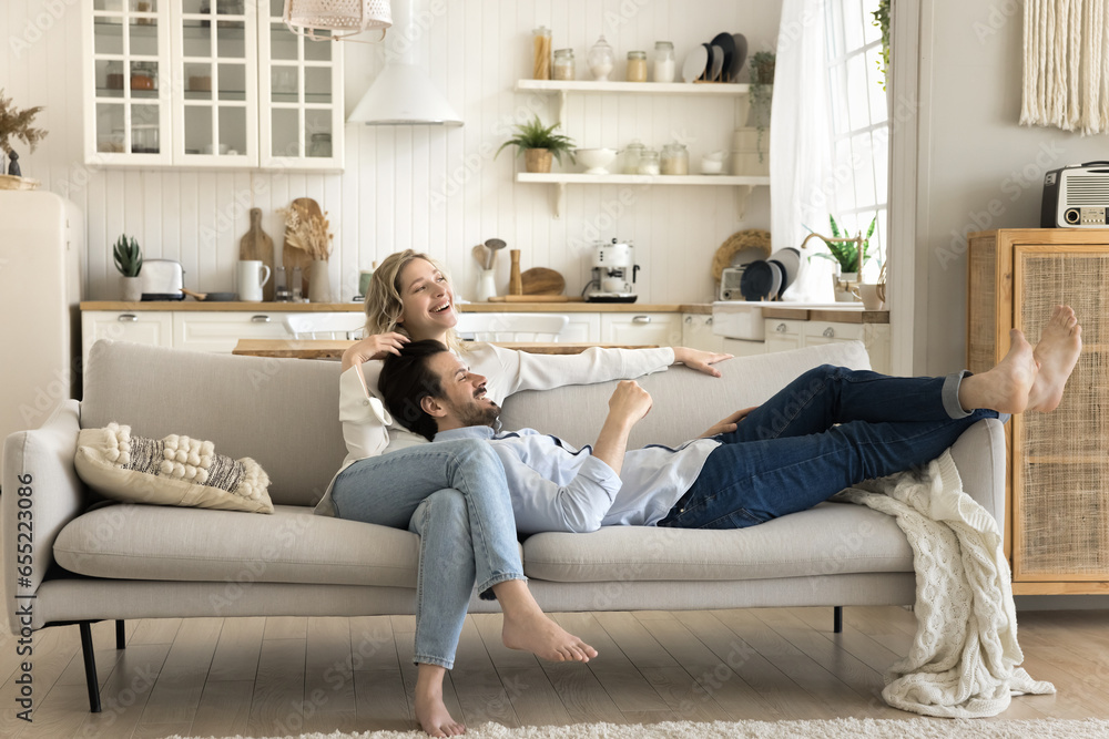 Beautiful married couple resting on couch, looking aside, daydreaming about their happy life, relish weekend leisure enjoy talk, planning future or vacation together at own or rented studio apartment - obrazy, fototapety, plakaty 