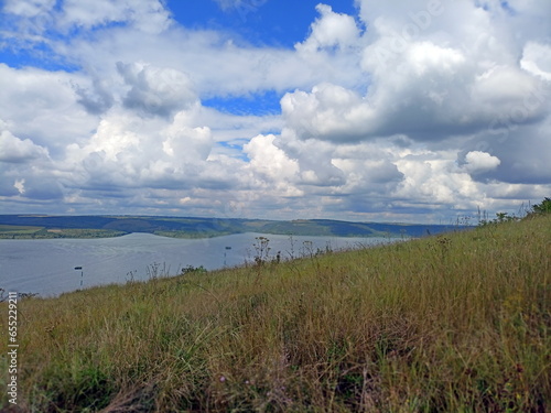 View from the slope of the hill covered with abundant green vegetation on the wide channel of the Dniester under snow-white summer clouds.