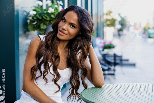 Beautiful portrait of an American girl with long curly hair sitting on a flyer in a cafe. Black woman smiling outdoors      