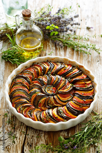Ratatouille from sliced colorful vegetables in a baking dish on a wooden table, close-up view