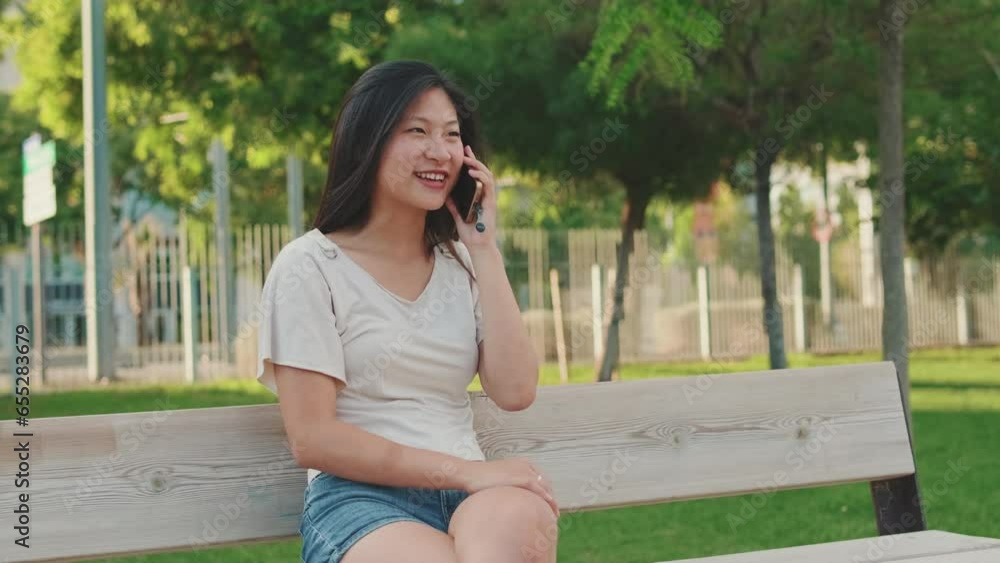 Joyful young woman sitting on bench in city park, talking on mobile phone Joyful young woman sitting on bench in city park, talking on mobile phone