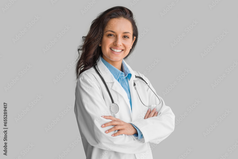 Cheerful young lady wearing white coat with stethoscope, doctor posing over grey background and smiling at camera Cheerful young lady wearing white coat with stethoscope, doctor posing over grey background and smiling at camera