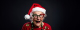 Studio portrait of eccentric elderly granny with toothless grin and holiday spirit, dressed up in Christmas outfit with ugly sweater, ornaments, and Santa hat