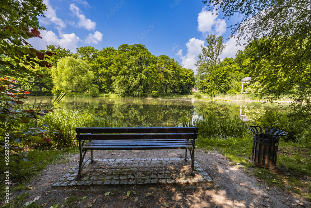 Old wooden bench in beautiful and colorful park at sunny morning with blue sky with few clouds beautifully reflecting in big silent lake like in mirror Old wooden bench in beautiful and colorful park at sunny morning with blue sky with few clouds beautifully reflecting in big silent lake like in mirror