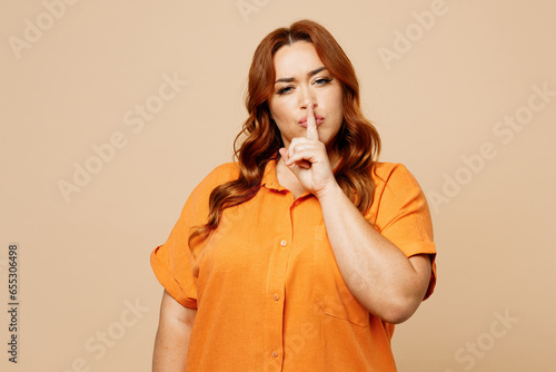 Young secret chubby overweight woman she wear orange shirt casual clothes say hush be quiet with finger on lips shhh gesture isolated on plain light beige background studio portrait Lifestyle concept. photo