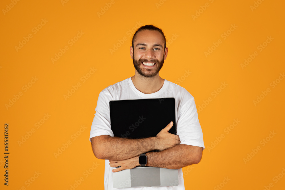 Happy adult european guy with beard in white t-shirt hugs laptop with blank screen, enjoy freelance