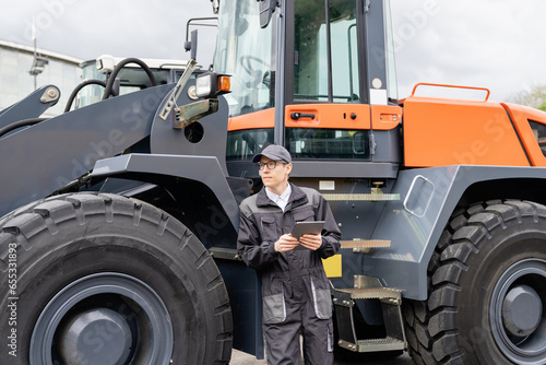 Serviceman with digital tablet on a background of the tractor. © scharfsinn86