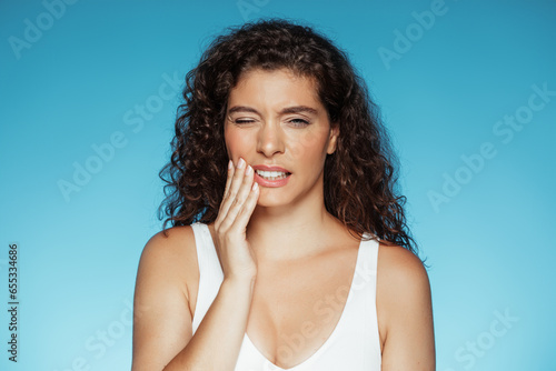 Photos Sad millennial european curly lady puts hand to cheek, suffering from toothache