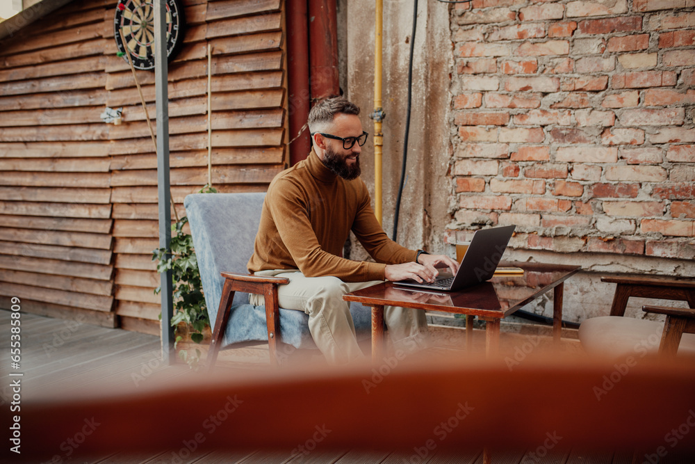 A stylish male freelancer is working on a new startup project, analyzing data using a laptop and a 5G wireless internet connection in a city cafe on a summer terrace with a free Wi-Fi zone