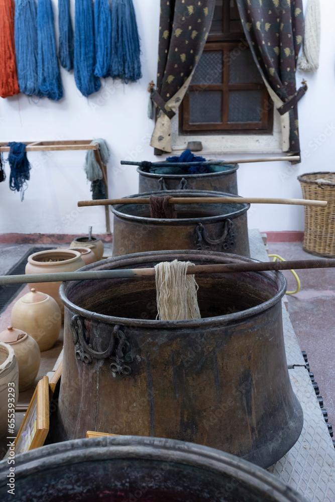 selective focus os a pots for the handmade dyeing of wool or silk, with pots with natural products for dyeing, and skeins of wool already dyed hanging on the wall, vertical selective focus os a pots for the handmade dyeing of wool or silk, with pots with natural products for dyeing, and skeins of wool already dyed hanging on the wall, vertical