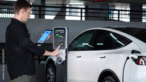 Young man travel with EV electric car to shopping center parking lot charging in downtown city showing urban sustainability lifestyle by green clean rechargeable energy of electric vehicle innards