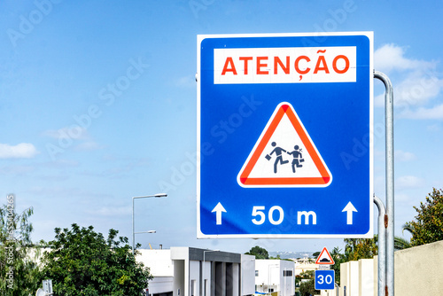 A Portuguese language, warning road sign, to advise that children are crossing the road, school nearby.