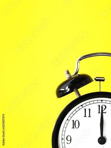 Black retro alarm clock at 12 twelve o clock on a yellow bakground with copy space to add text 12am 12pm photo