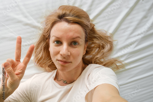 Young happy woman taking selfie portrait while resting on the bed at morning. Portrait of self-assured authentic woman feeling great accepting own imperfections 