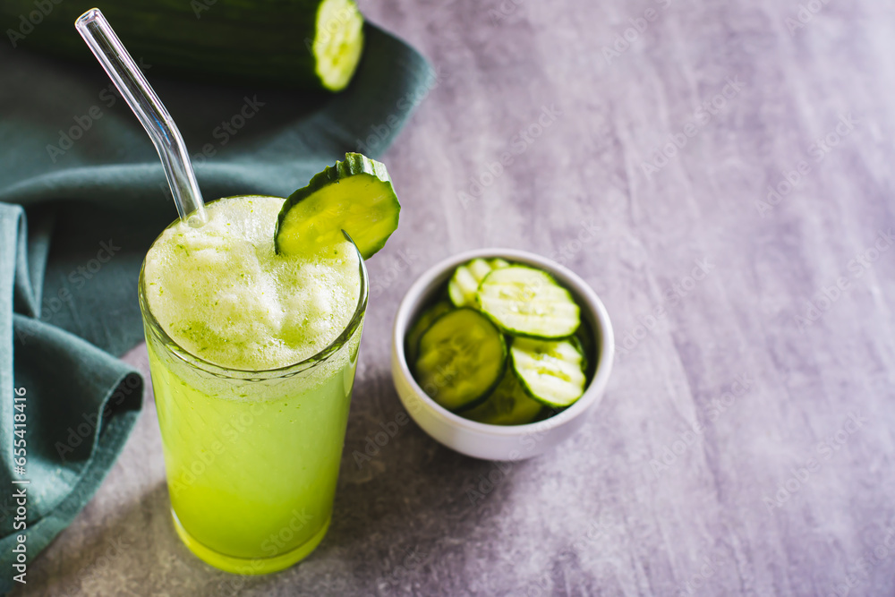 Fototapeta premium Detox cucumber lemonade in a glass with a straw and a cucumber on the table
