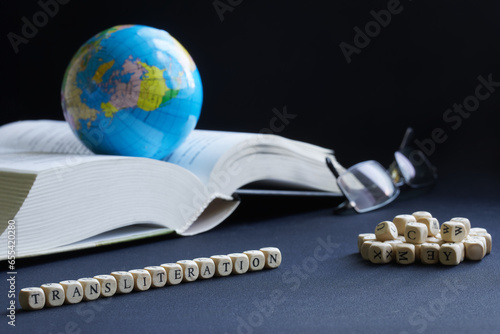 Transliteration inscription next to an open book, globe and glasses. The concept of educational work on translation and transliteration of texts. Selective focus. Photo