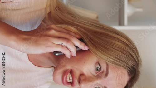 Vertical video. Unhappy call. Mobile phone talking. Disturbed worried woman arguing on smartphone unpleasant communication in light room interior. photo