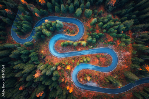 Aerial view of snake road in colorful autumn forest at sunrise. Dolomites, Italy. Top view of winding road in woods. Beautiful landscape with highway, green pine trees, red leaves in fall. Nature