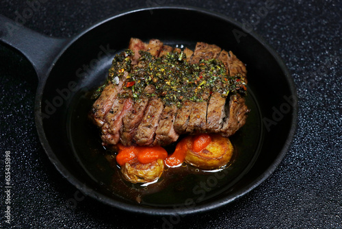 spanish chimichurri beef steaks with potato and spicy brava sauce in black background