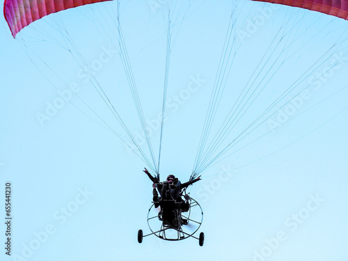 Men fly on a paraglider with a motor. The man, a rock lover, spreads his arms to the sides and shows a rocking gesture. Close-up.