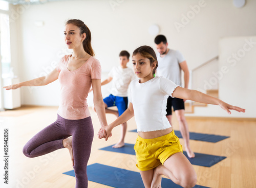 Focused teenage girl exercising with mother at couple yoga class while her father practicing with her brother