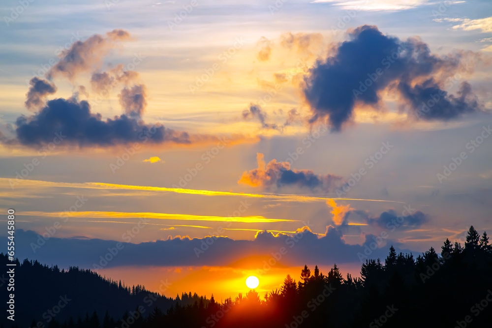 Fototapeta premium Colorful clouds in the sky at sunset against the backdrop of a mountainous forest area.