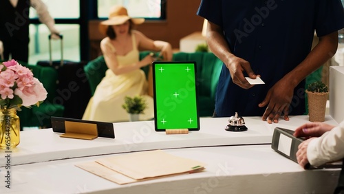 Hotel concierge service with greenscreen, modern tropical resort front desk with isolated mockup template on digital tablet. Receptionist working in hotel lobby with blank copyspace.