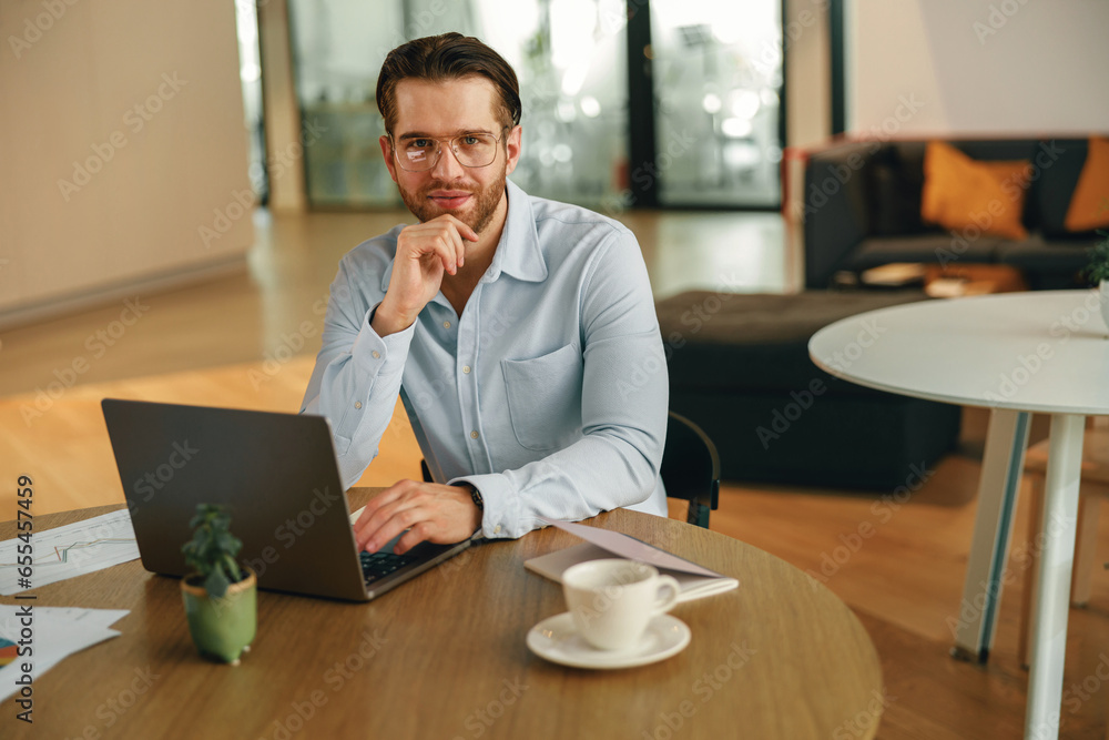 Male manager drinking coffee during working on laptop in modern office . High quality photo Male manager drinking coffee during working on laptop in modern office . High quality photo