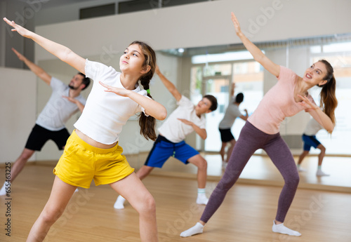 Girl dancing modern dance with family during group rehearsal in gym.