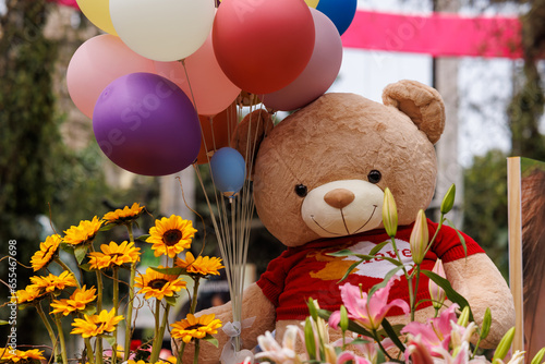 Teddy bear with balloons and flowers of many colors
