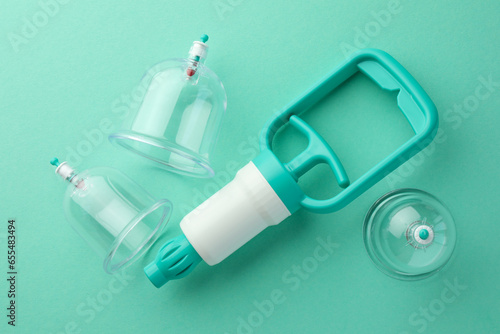 Plastic cups and hand pump on turquoise background, flat lay. Cupping therapy