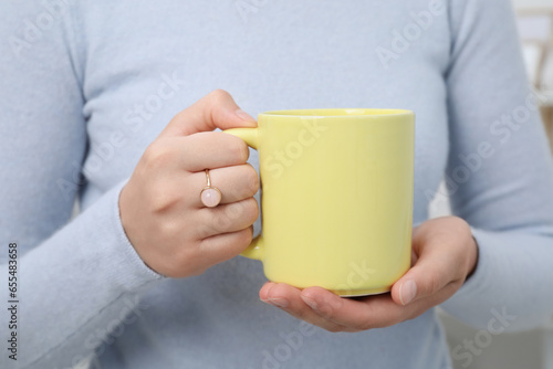 Closeup view of woman holding yellow mug. Mockup for design